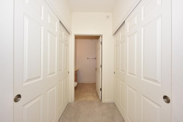 corridor with baseboards, light tile patterned floors, and light colored carpet