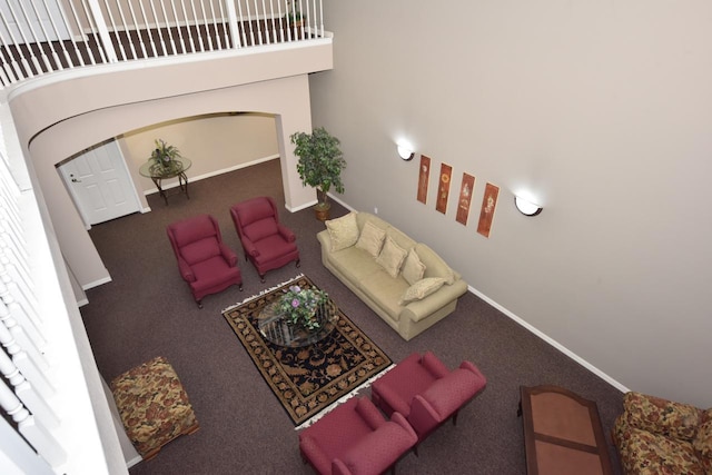 carpeted living area with arched walkways, a high ceiling, and baseboards