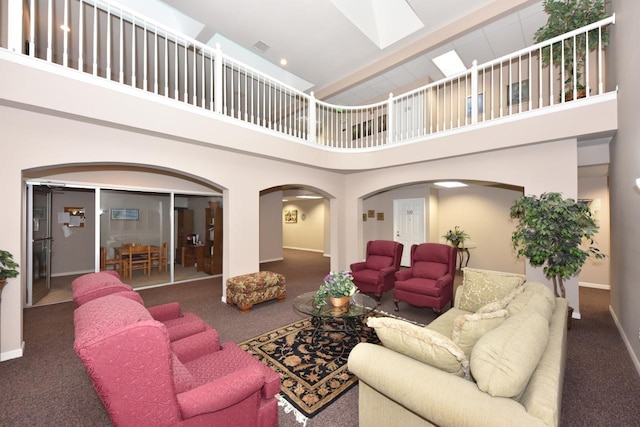 living area with a towering ceiling, a skylight, arched walkways, and carpet flooring