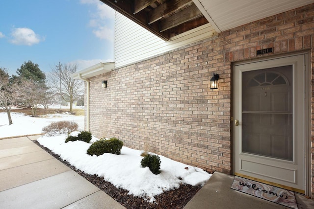 snow covered property entrance featuring brick siding