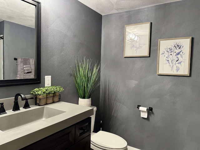 bathroom with a textured wall, vanity, and toilet