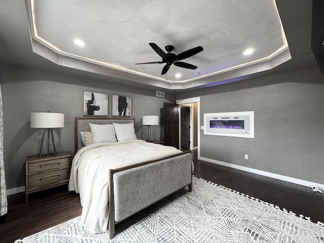 bedroom with a raised ceiling, visible vents, baseboards, and wood finished floors