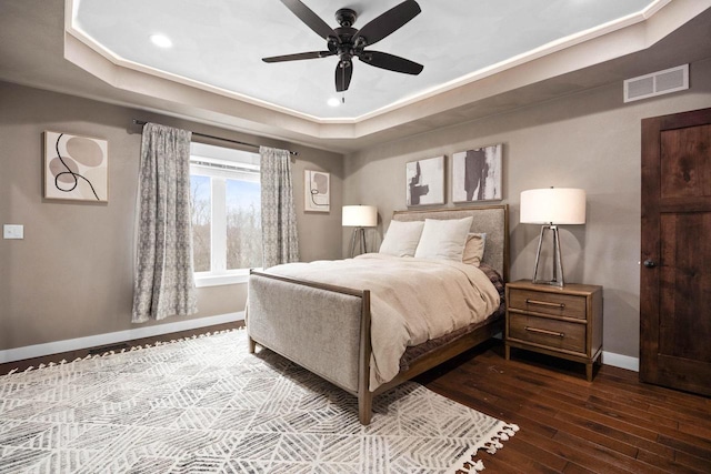 bedroom featuring dark wood-style flooring, a raised ceiling, visible vents, a ceiling fan, and baseboards