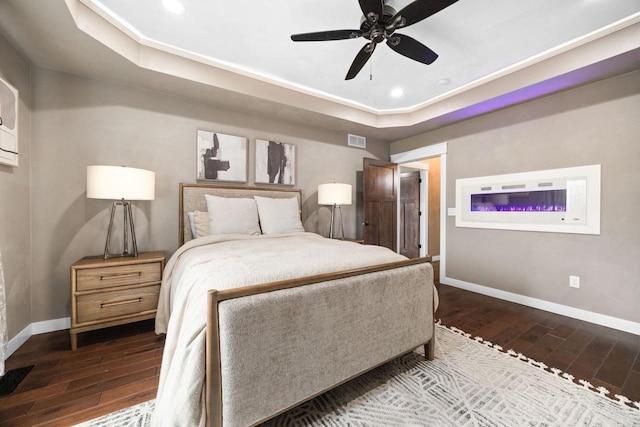 bedroom with a tray ceiling, dark wood-type flooring, visible vents, and baseboards