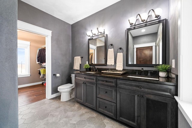 full bathroom with baseboards, a sink, toilet, and double vanity