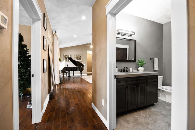 hallway featuring lofted ceiling, a sink, baseboards, and wood finished floors