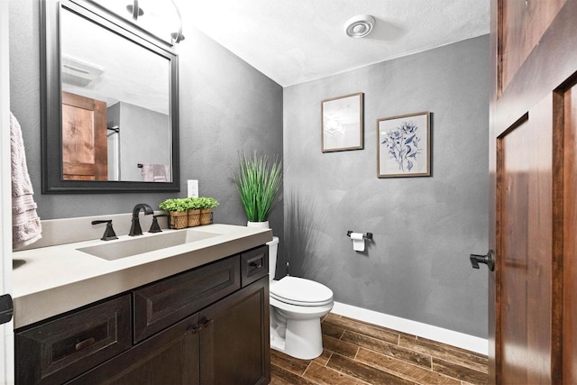 bathroom with wood finish floors, a textured wall, toilet, vanity, and baseboards