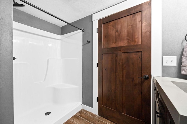 bathroom with a shower, wood finish floors, vanity, and baseboards