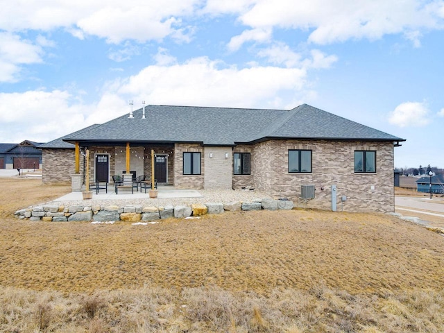 back of house featuring central air condition unit, a patio area, brick siding, and roof with shingles