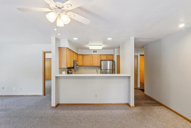 kitchen featuring a peninsula, a ceiling fan, baseboards, light countertops, and freestanding refrigerator