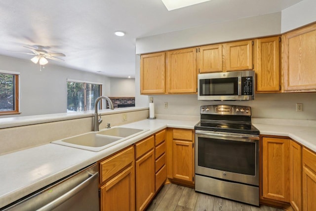 kitchen with wood finished floors, a peninsula, stainless steel appliances, light countertops, and a sink