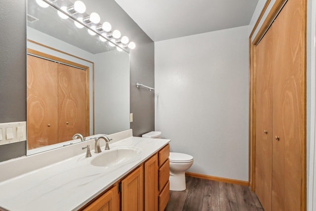 bathroom with baseboards, toilet, wood finished floors, vanity, and a closet