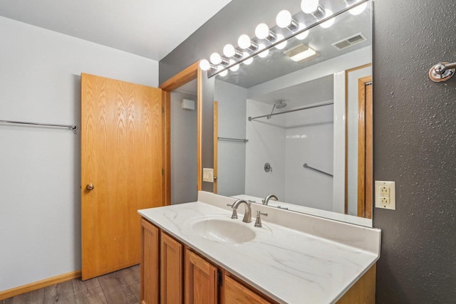 bathroom with wood finished floors, vanity, visible vents, baseboards, and walk in shower