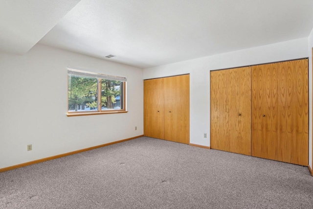 unfurnished bedroom featuring carpet, two closets, visible vents, and baseboards