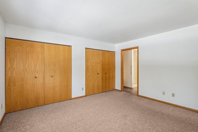 unfurnished bedroom with carpet, two closets, and baseboards