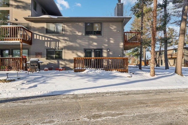 snow covered rear of property featuring a chimney and a wooden deck