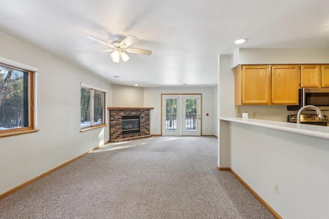 unfurnished living room with baseboards, ceiling fan, a brick fireplace, and light colored carpet