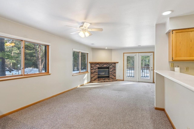 unfurnished living room featuring a ceiling fan, a brick fireplace, light colored carpet, and baseboards