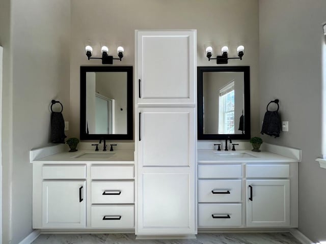 full bathroom with marble finish floor, double vanity, a sink, and baseboards