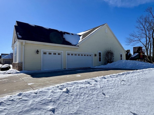 view of snowy exterior with a playground and an attached garage