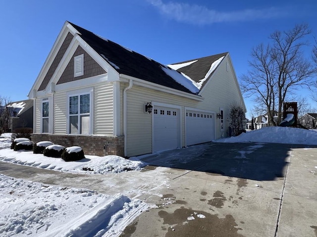 view of snow covered exterior featuring a garage, brick siding, and driveway