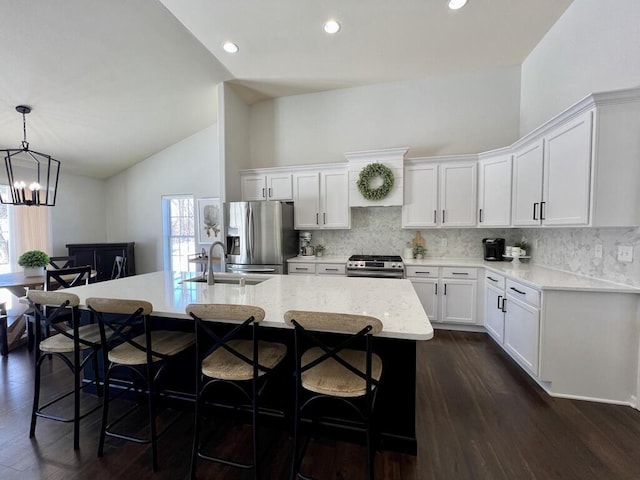 kitchen with a center island with sink, white cabinets, appliances with stainless steel finishes, hanging light fixtures, and a sink