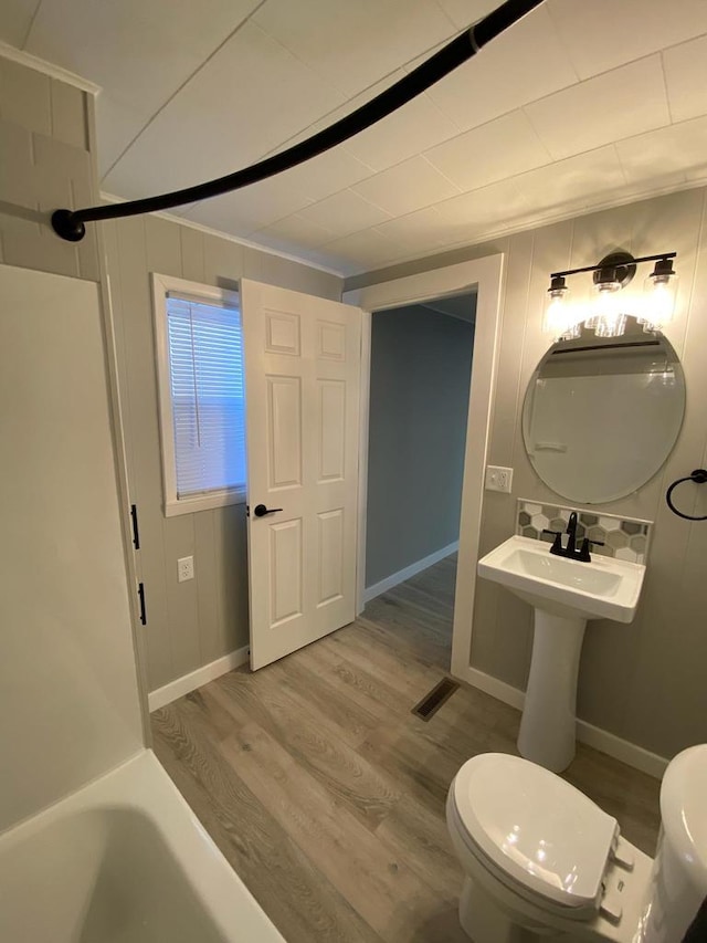 bathroom with baseboards, visible vents, toilet, wood finished floors, and a bathtub