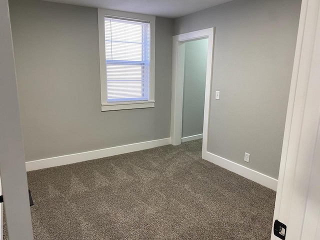 spare room with dark colored carpet and baseboards