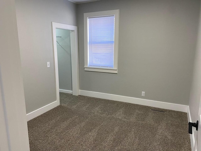 unfurnished room featuring dark carpet, visible vents, and baseboards