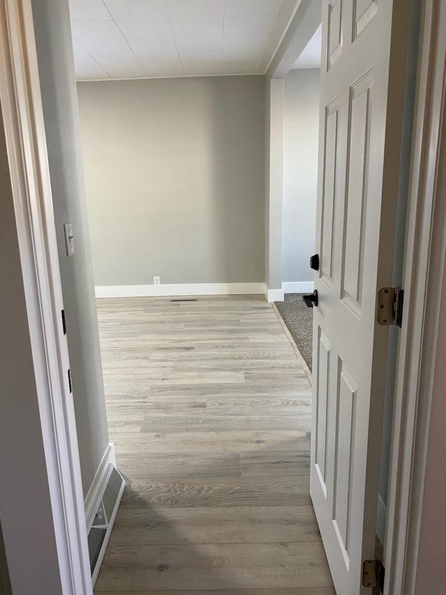 hallway with light wood-type flooring, visible vents, and baseboards