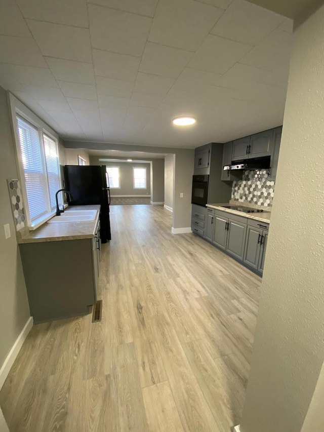 kitchen with black appliances, gray cabinets, under cabinet range hood, and light countertops