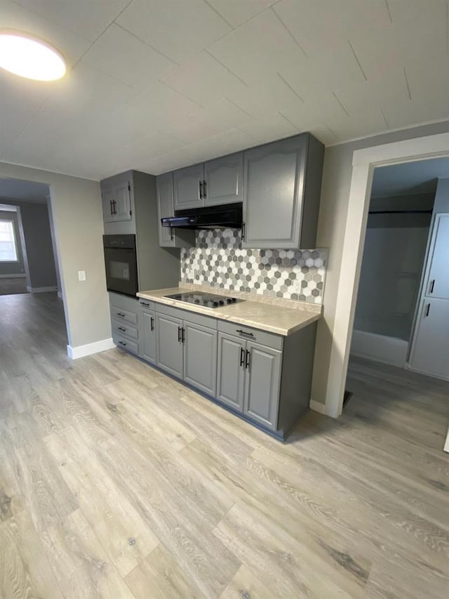 kitchen featuring light wood-style flooring, under cabinet range hood, light countertops, gray cabinetry, and black appliances