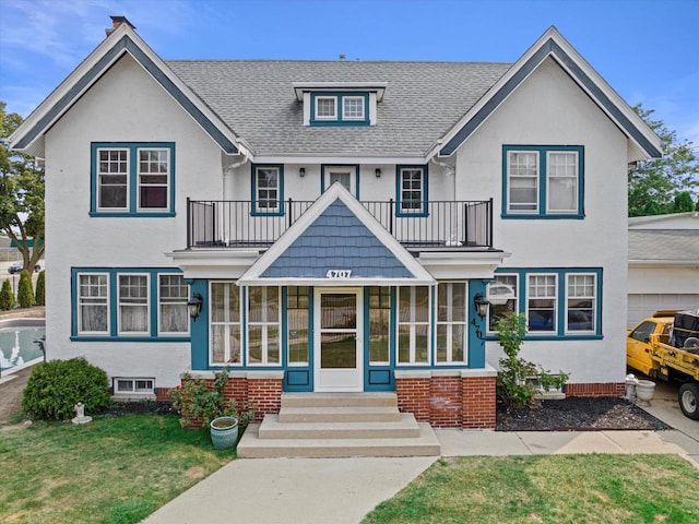 view of front facade featuring a front yard, roof with shingles, a balcony, and stucco siding