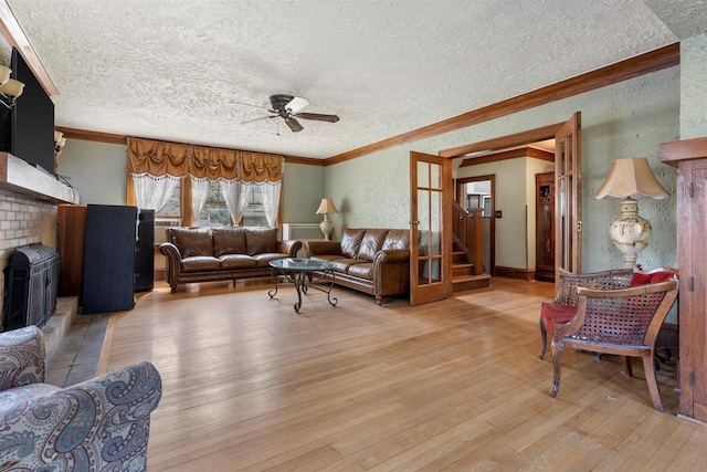 living room featuring a textured wall, light wood-style flooring, ceiling fan, crown molding, and a brick fireplace