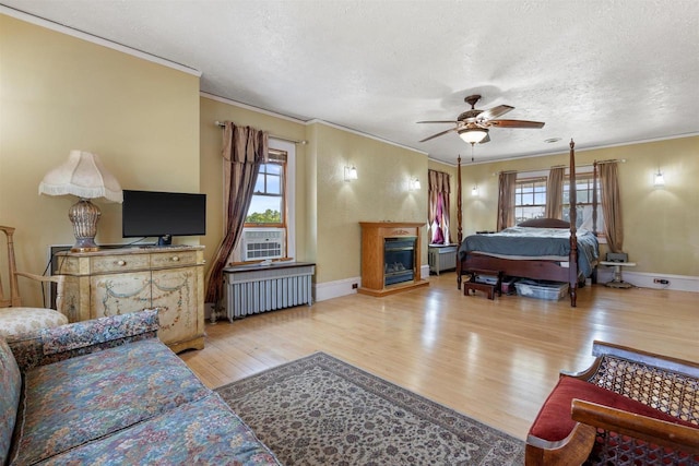 bedroom with multiple windows, radiator heating unit, light wood-type flooring, and a glass covered fireplace