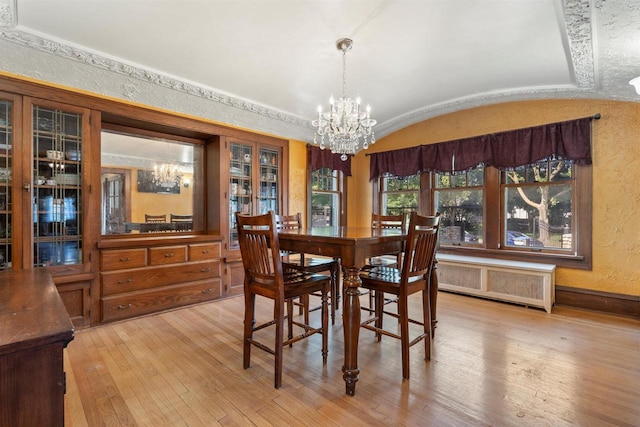 dining space featuring radiator, a textured wall, an inviting chandelier, vaulted ceiling, and wood finished floors