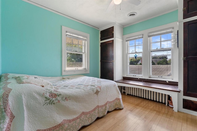 bedroom featuring visible vents, a ceiling fan, radiator, ornamental molding, and light wood-style floors