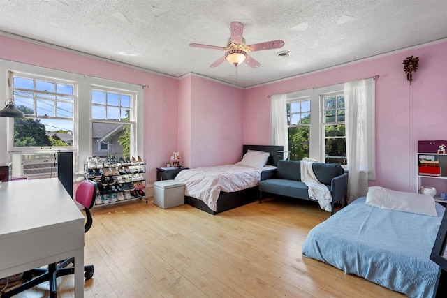 bedroom featuring light wood-type flooring, visible vents, multiple windows, and a textured ceiling