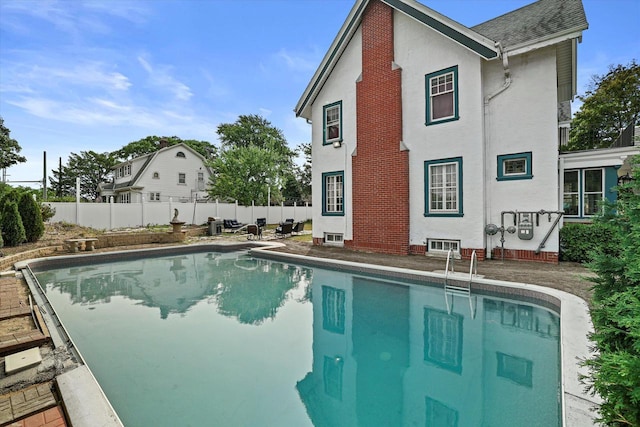 rear view of house with a fenced in pool, roof with shingles, fence, and stucco siding