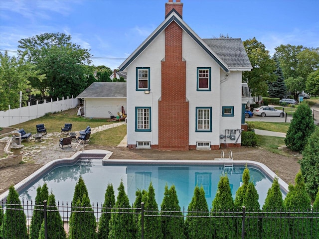 rear view of house with a fenced in pool, a chimney, roof with shingles, fence, and stucco siding