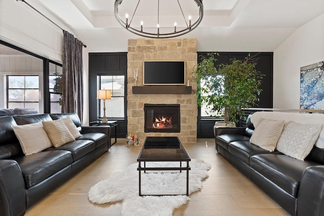 living room with a stone fireplace, light wood-type flooring, and an inviting chandelier