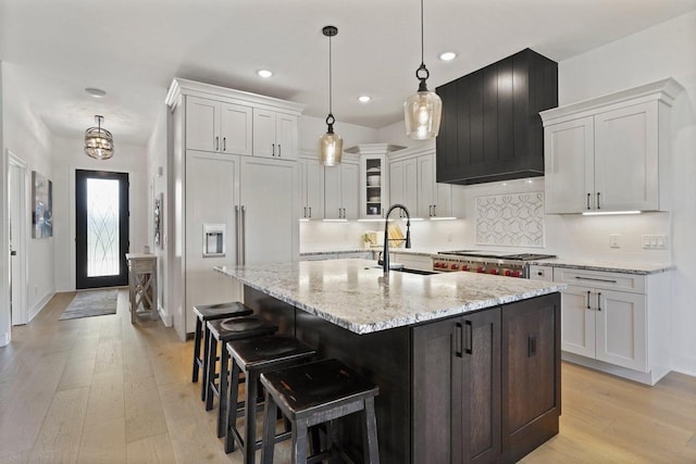 kitchen with a center island with sink, stainless steel gas stovetop, glass insert cabinets, white cabinetry, and a sink