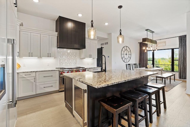 kitchen with hanging light fixtures, premium appliances, an island with sink, and white cabinetry