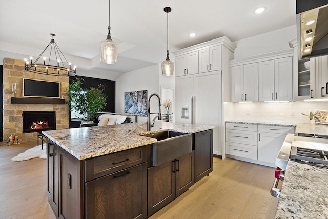 kitchen with pendant lighting, light wood-style flooring, glass insert cabinets, white cabinetry, and a sink