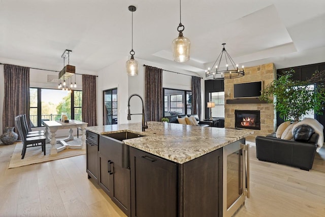 kitchen with a tray ceiling, decorative light fixtures, a center island with sink, open floor plan, and beverage cooler