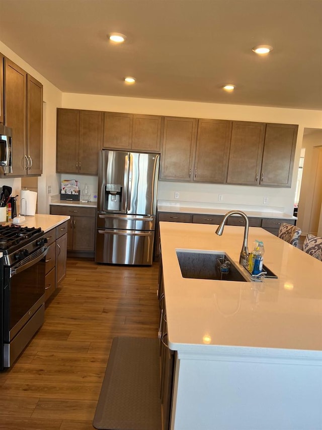 kitchen featuring recessed lighting, light countertops, appliances with stainless steel finishes, dark wood-type flooring, and a sink