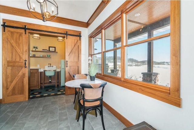 dining space with a chandelier, a barn door, crown molding, and baseboards