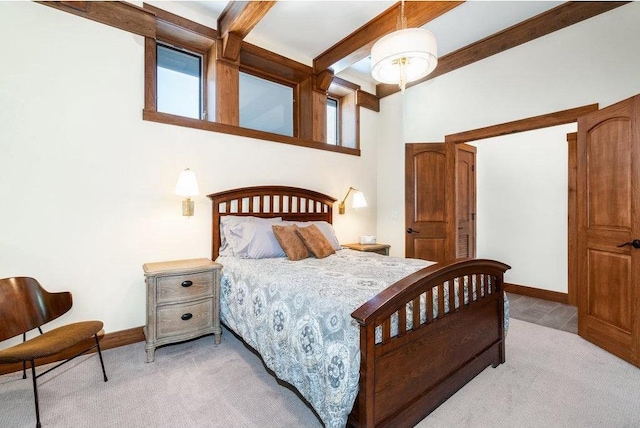 bedroom with beam ceiling, light carpet, and baseboards