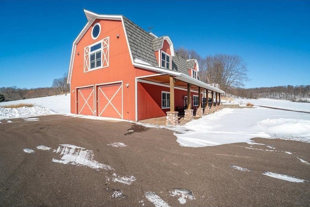 view of snowy exterior featuring a barn, a garage, an outbuilding, and a gambrel roof