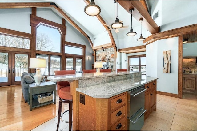 kitchen featuring a breakfast bar, french doors, hanging light fixtures, brown cabinetry, and open floor plan